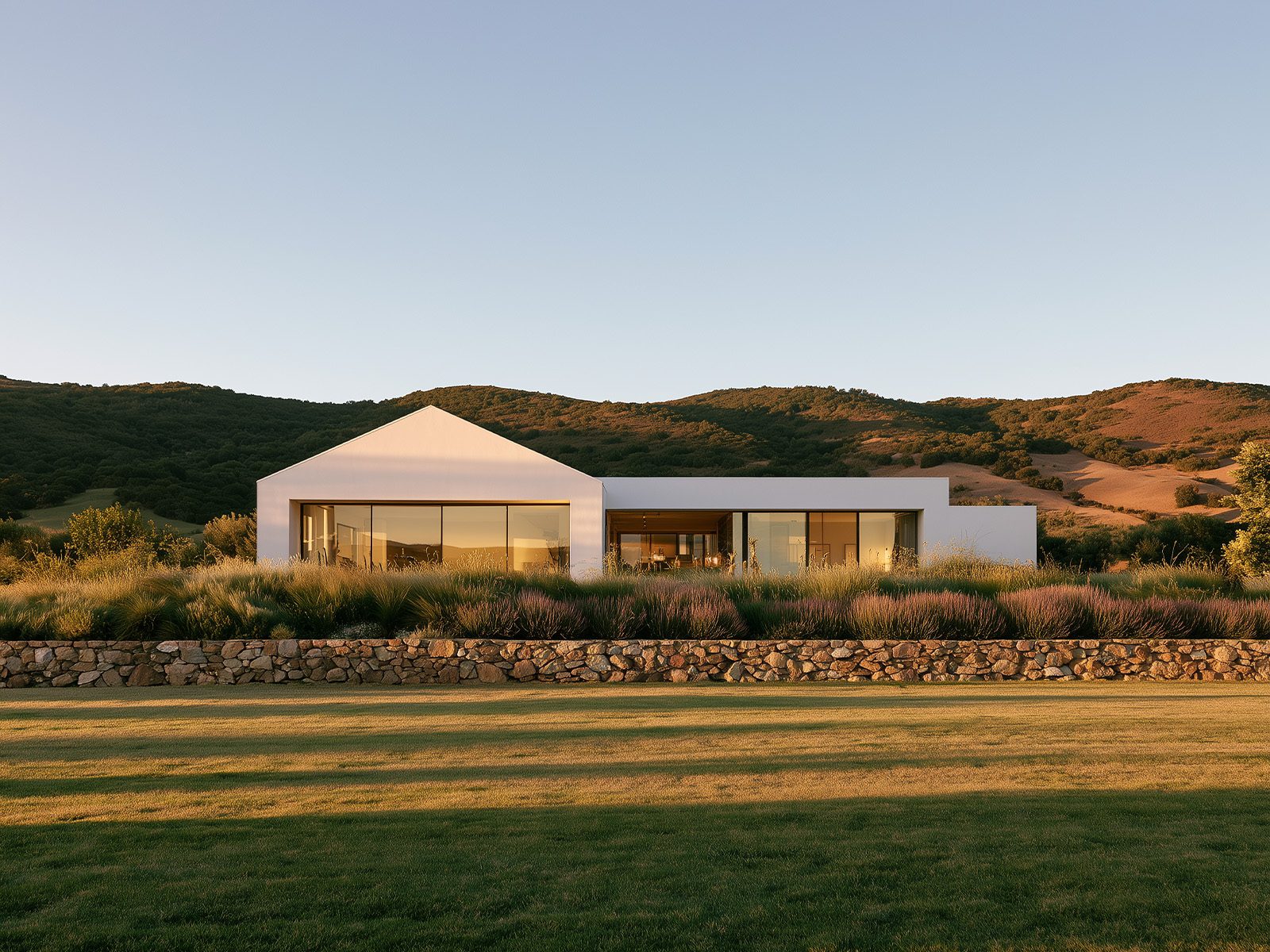 Modern house in open landscape with hills and vegetation behind a stone wall