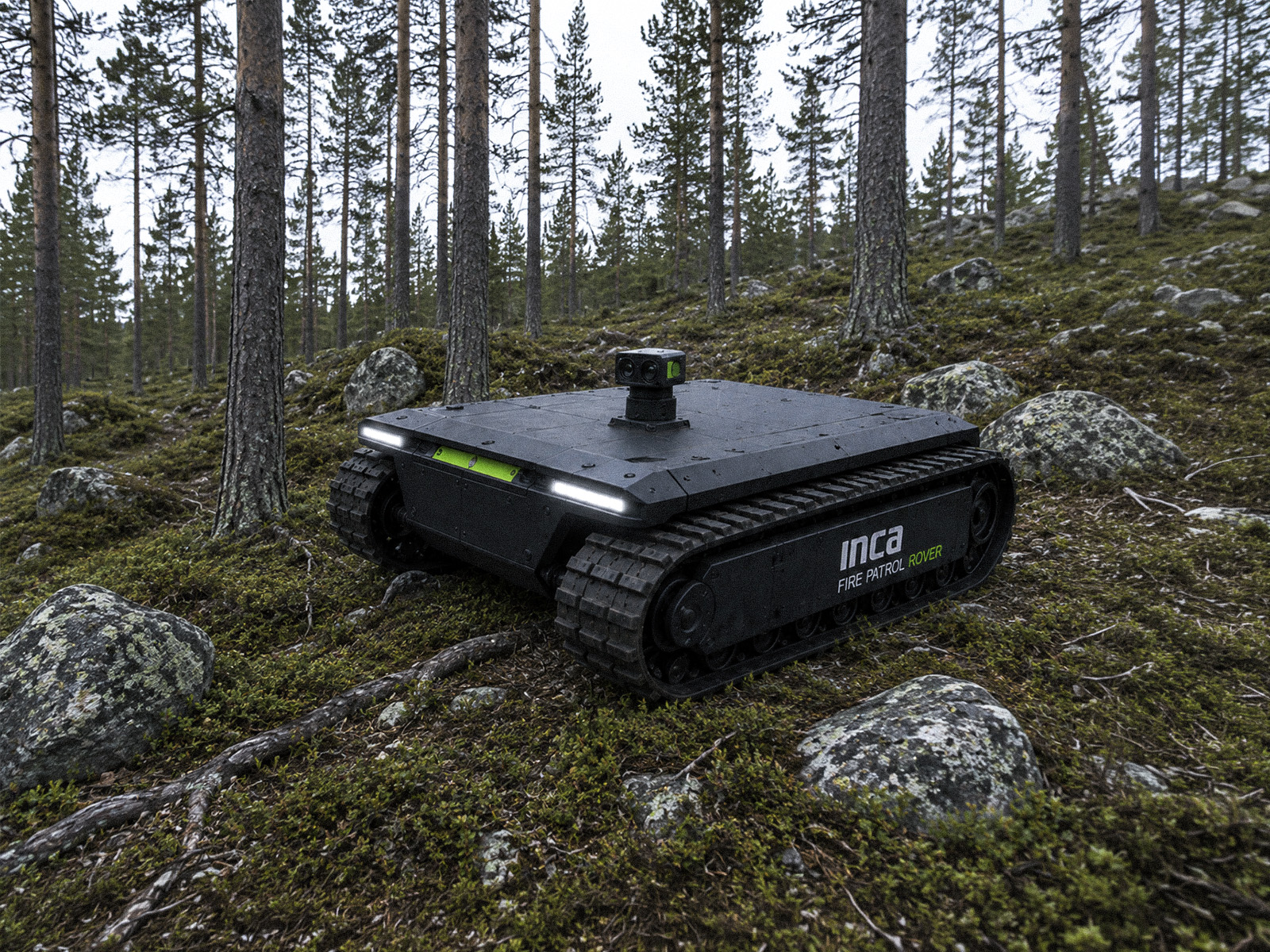 INCA Fire Patrol Rover, a tracked unmanned ground vehicle, standing on mossy forest ground among pine trees.