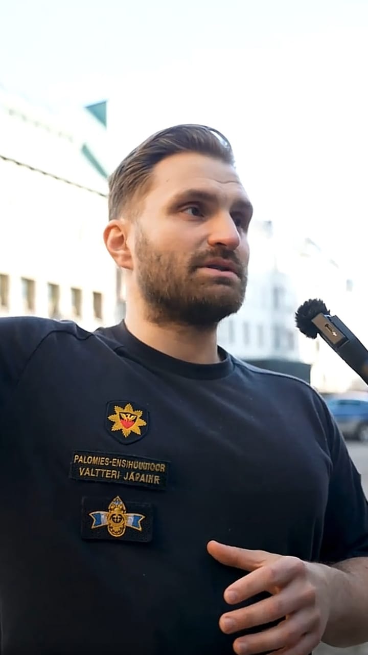 Finnish firefighter in a black uniform T-shirt speaking into a microphone outdoors