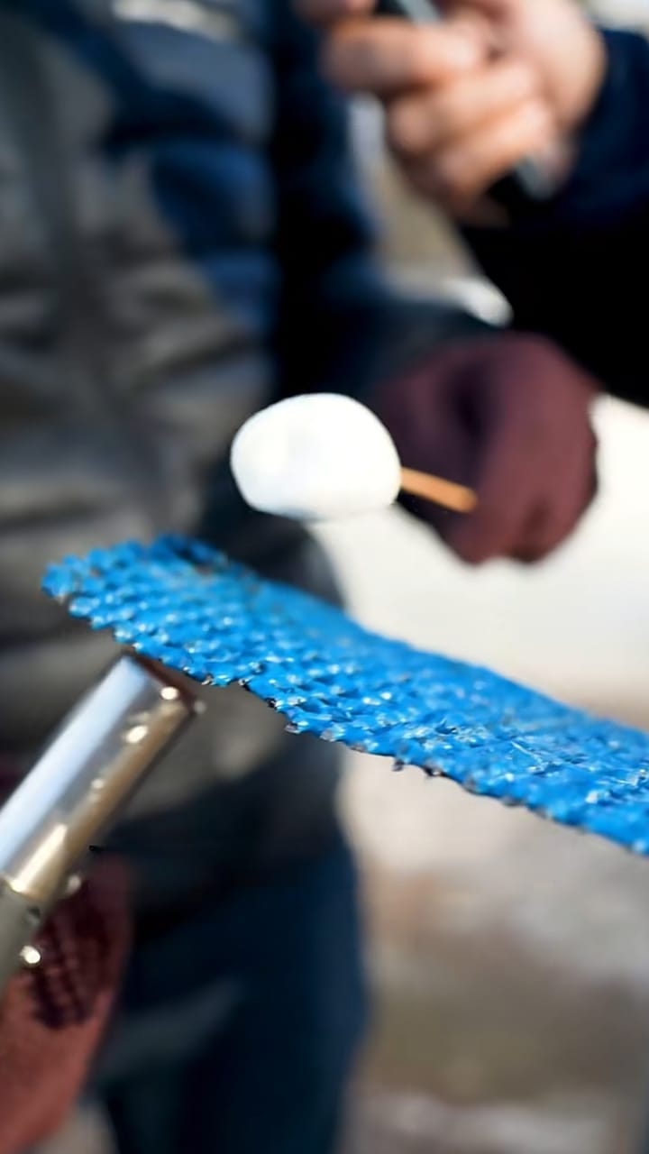 Gas torch aimed at a sheet of blue coated INCA WFS net® with a marshmallow held on the other side