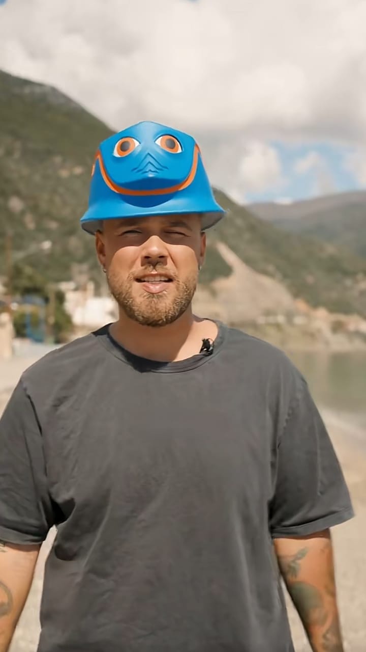 Presenter wearing a blue INCA helmet on a beach with green hills behind
