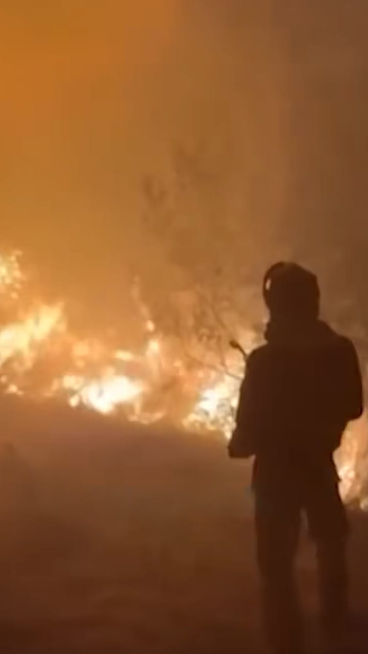 Firefighter silhouetted against a wildfire at night