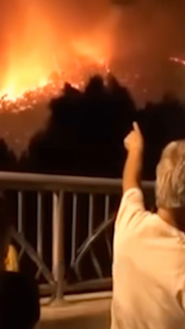 Person pointing at a wildfire burning on a hillside at night